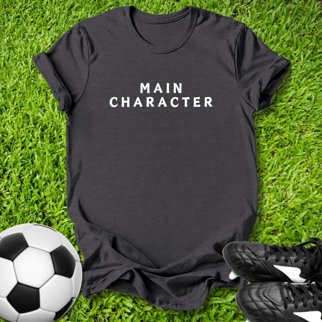 Black t-shirt with 'MAIN CHARACTER' text on grass with soccer ball and shoes