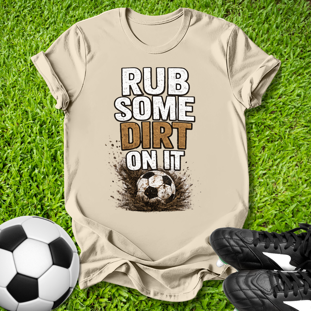 Natural  t-shirt with 'Rub some dirt on it' text on grass with soccer ball and shoes.