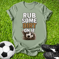 greent-shirt with 'Rub some dirt on it' text on grass with soccer ball and shoes.