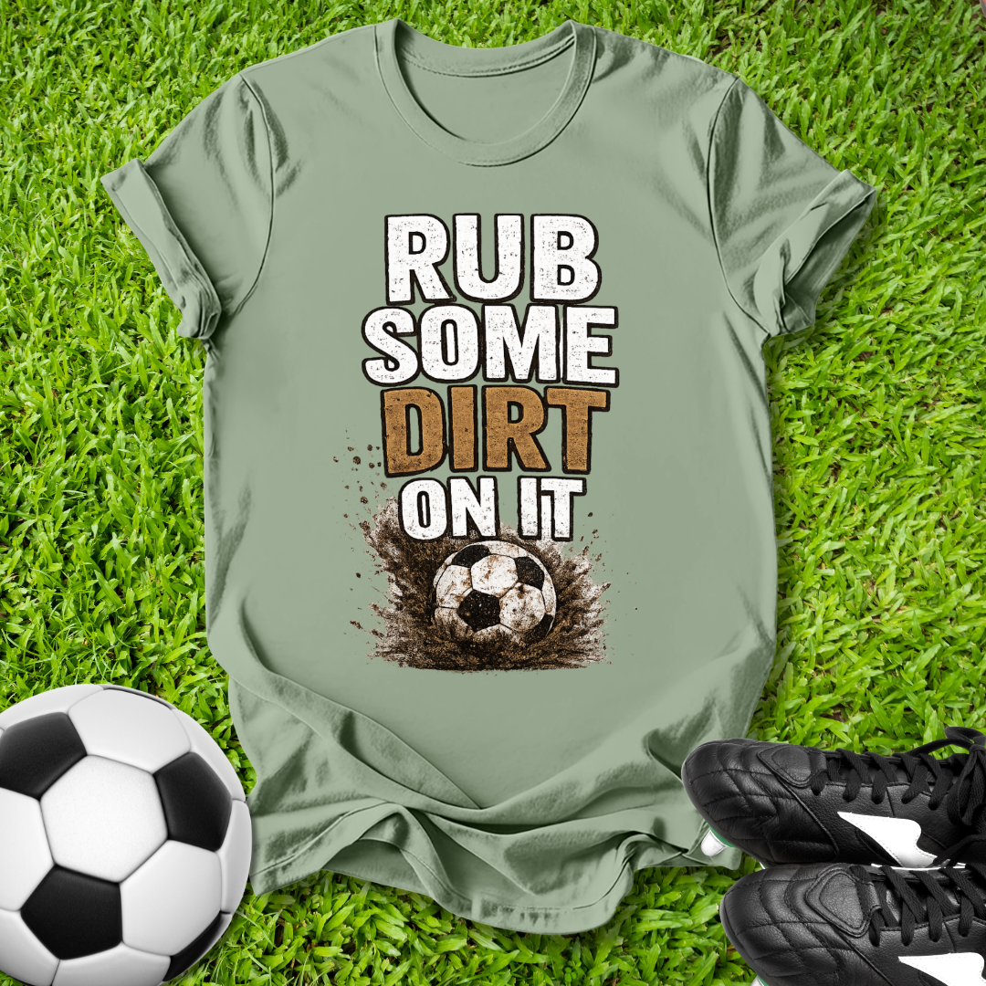 greent-shirt with 'Rub some dirt on it' text on grass with soccer ball and shoes.