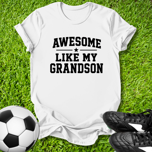 White blue t-shirt with 'Awesome like my grandson' text on grass with soccer ball and shoes.