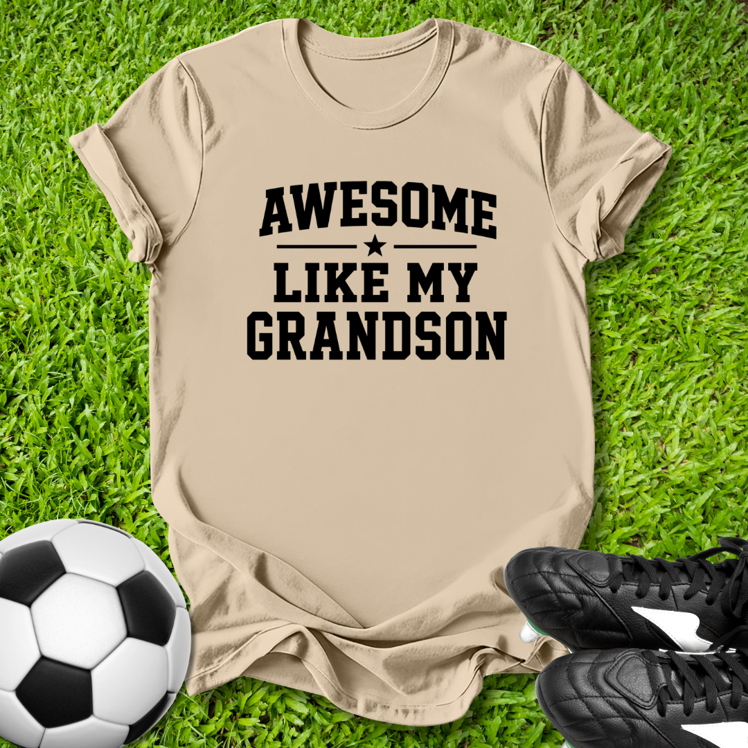 Beige t-shirt with 'Awesome Like My Grandson' text on grass with soccer ball and shoes.