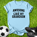 Light blue t-shirt with 'Awesome like my grandson' text on grass with soccer ball and shoes.