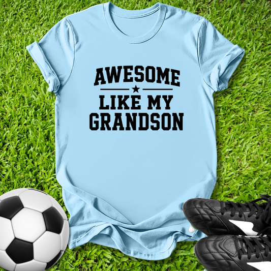 Light blue t-shirt with 'Awesome like my grandson' text on grass with soccer ball and shoes.