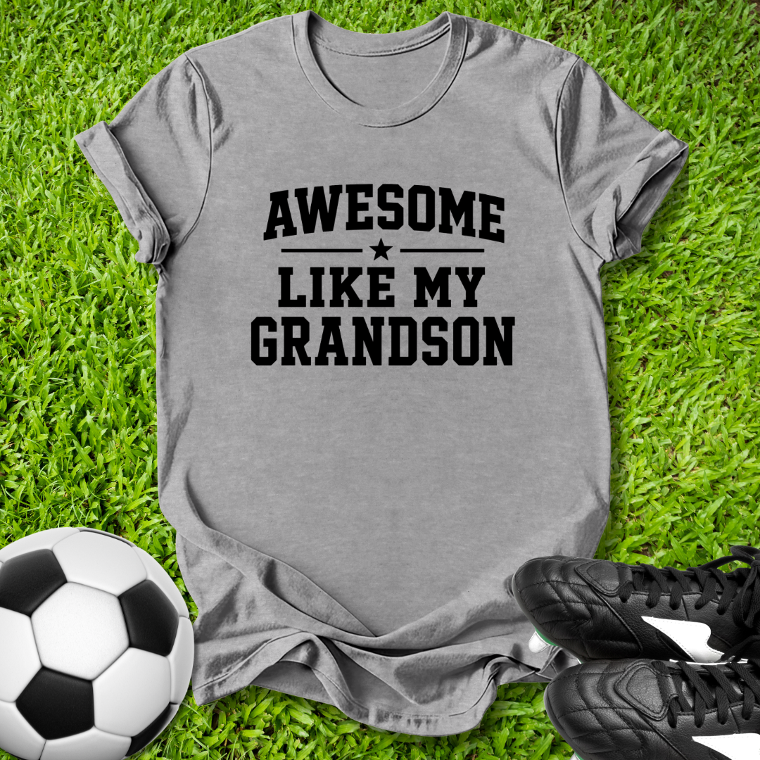 Gray t-shirt with 'Awesome like my grandson' text on grass with soccer ball and shoes.