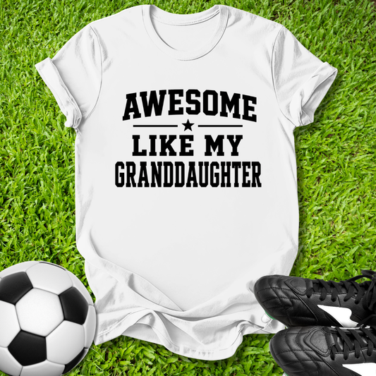 White t-shirt with 'Awesome Like My Granddaughter' text on grass with soccer ball and shoes.