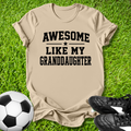 Beige t-shirt with 'Awesome Like My Grandson' text on grass with soccer ball and shoes.