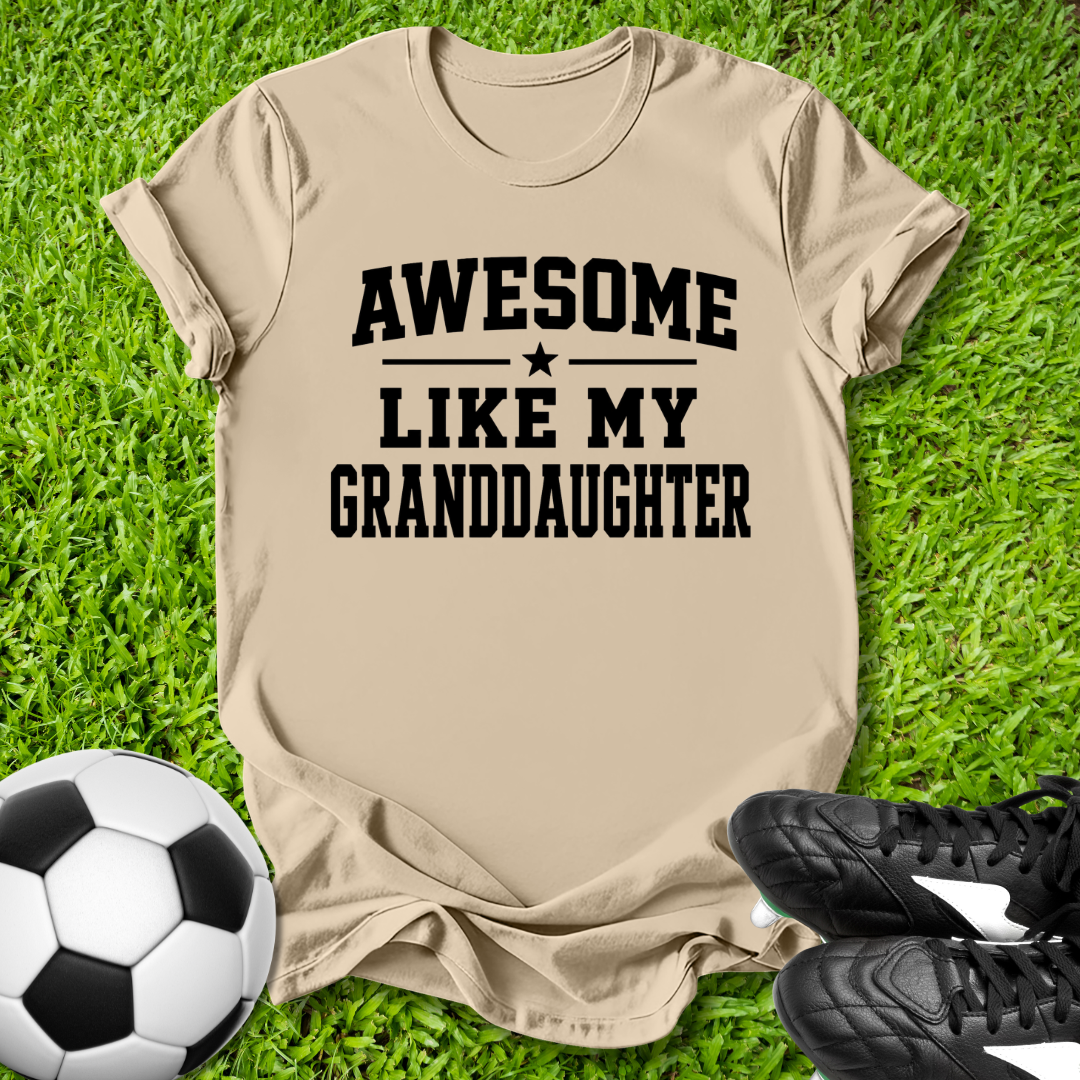 Beige t-shirt with 'Awesome Like My Grandson' text on grass with soccer ball and shoes.