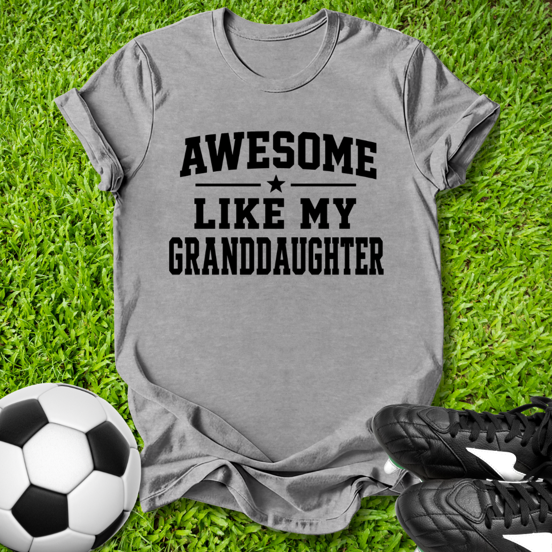 Gray t-shirt with 'Awesome like my granddaughter' text on grass with soccer ball and shoes.
