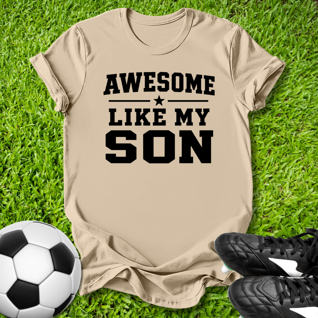 Beige t-shirt with 'Awesome Like My Son' text on grass with soccer ball and shoes.