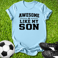 Light blue t-shirt with 'Awesome Like My Son' text on grass with soccer ball and shoes.
