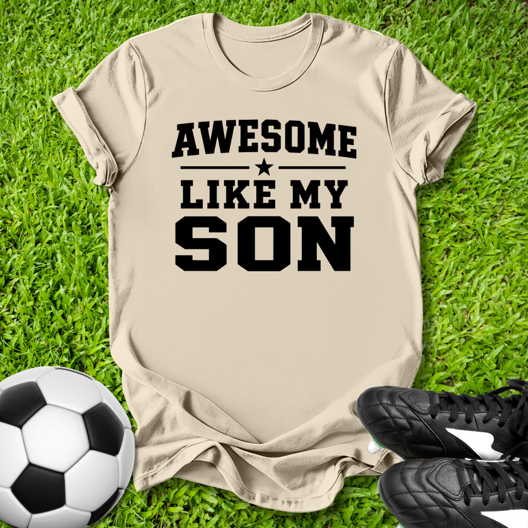 Beige t-shirt with 'Awesome Like My Son' text on grass with soccer ball and shoes.
