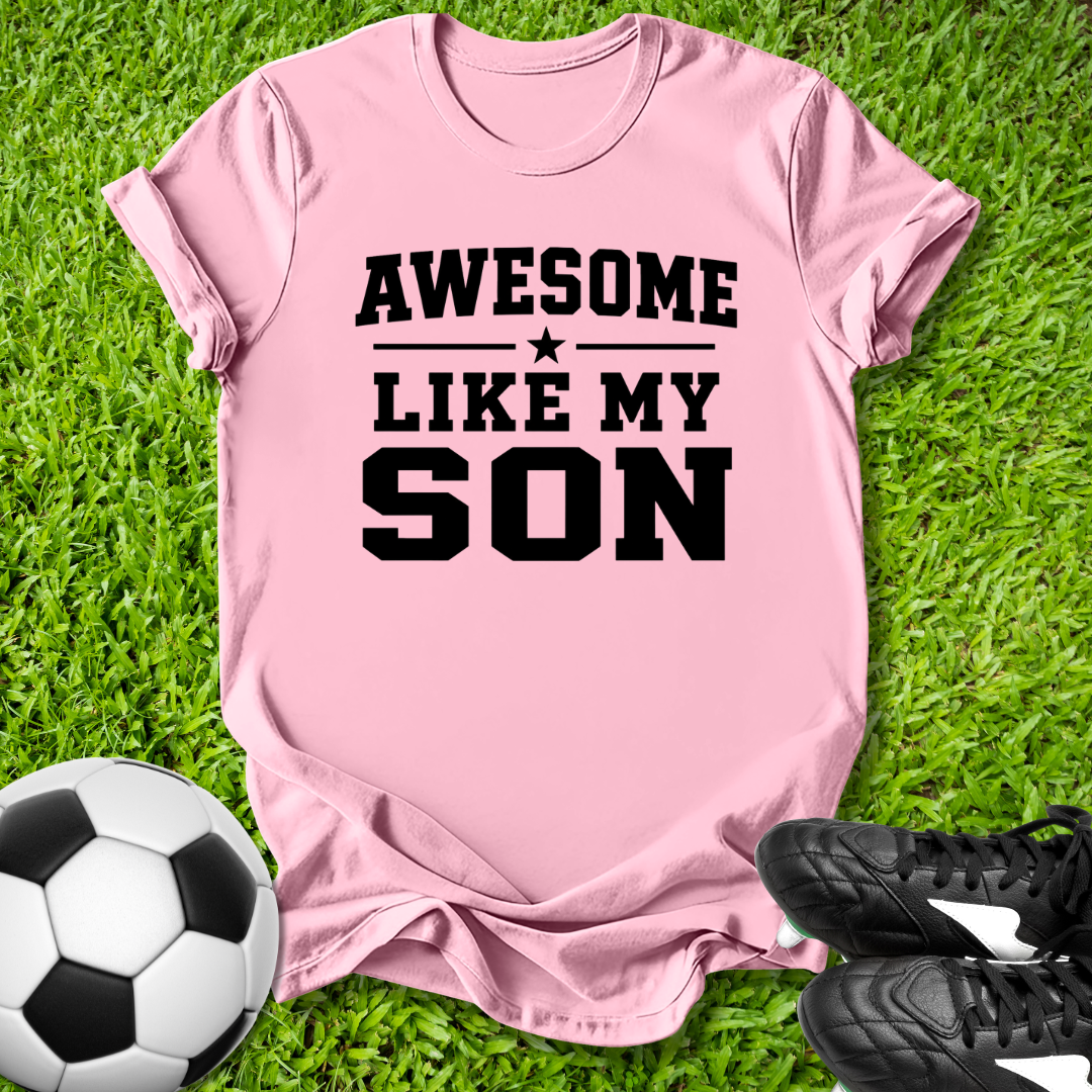 Pink t-shirt with 'Awesome Like My Son' text on grass with soccer ball and shoes.