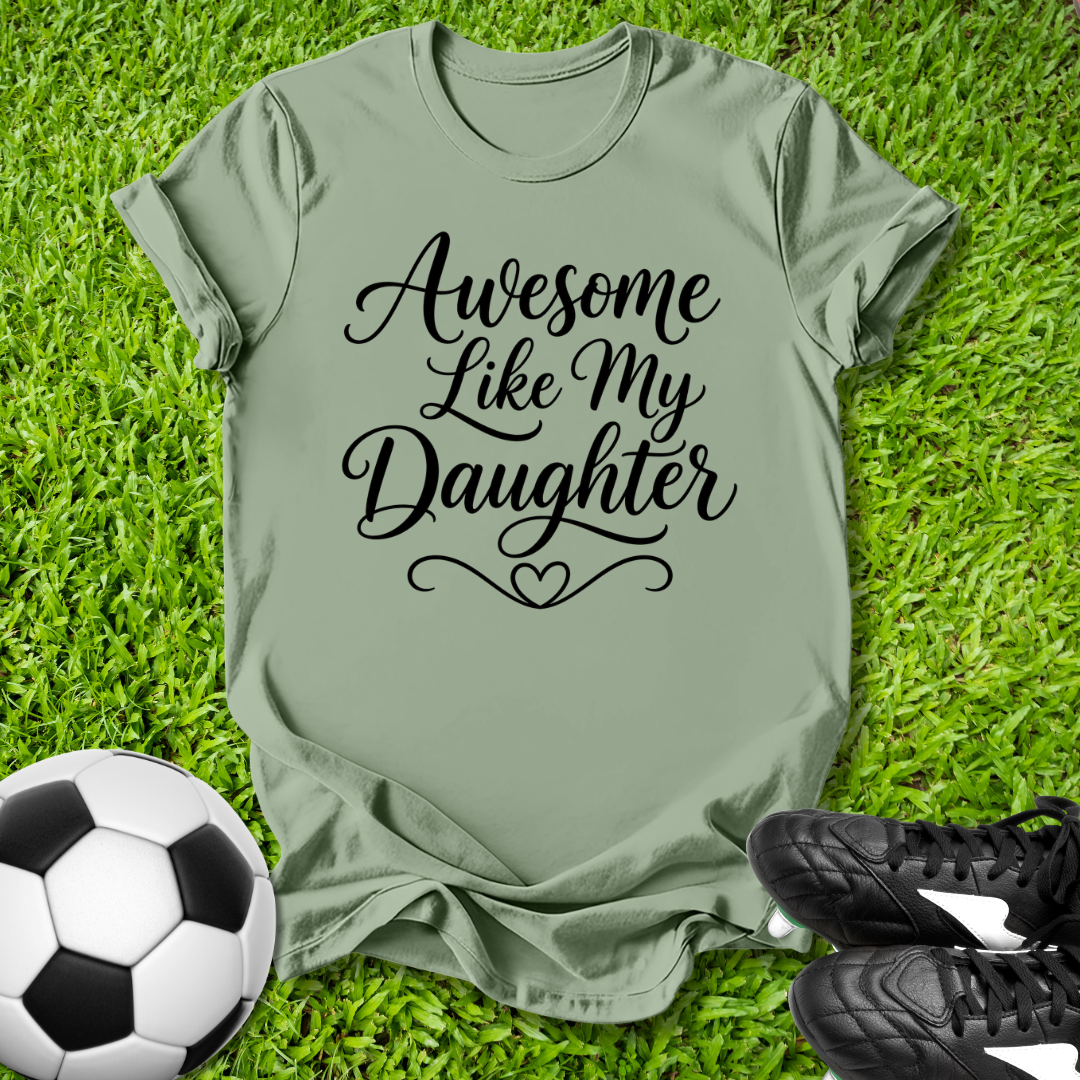 Green t-shirt with 'Awesome Like My Daughter' text on grass with soccer ball and shoes.