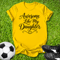 Yellow t-shirt with 'Awesome Like My Daughter' text on grass with soccer ball and shoes.