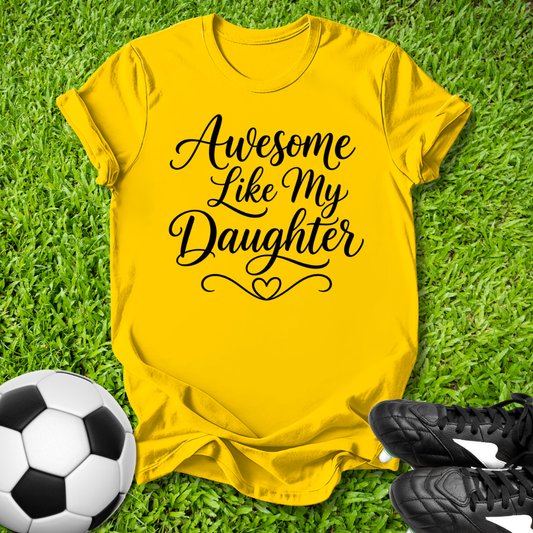 Yellow t-shirt with 'Awesome Like My Daughter' text on grass with soccer ball and shoes.