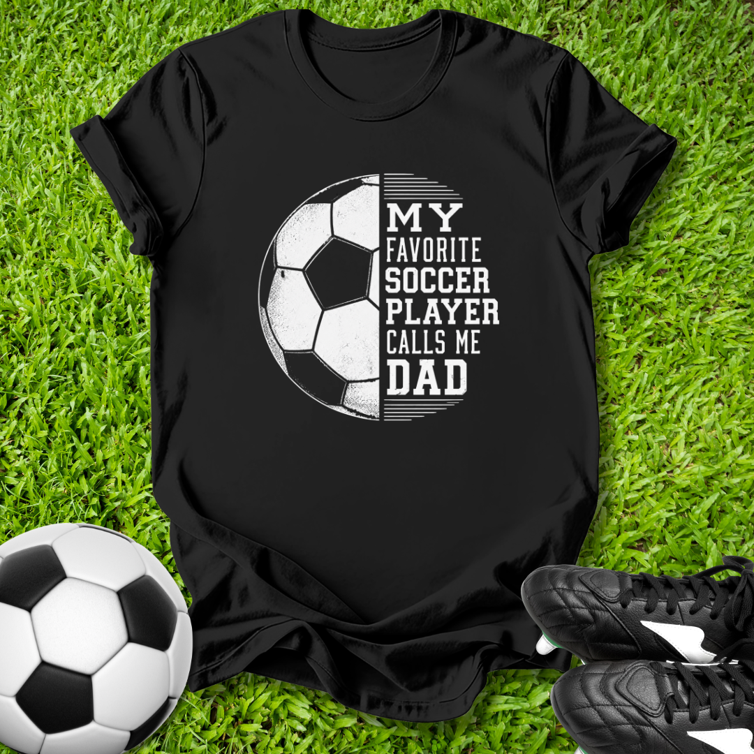 Black t-shirt with soccer design and text on grass with soccer ball and shoes