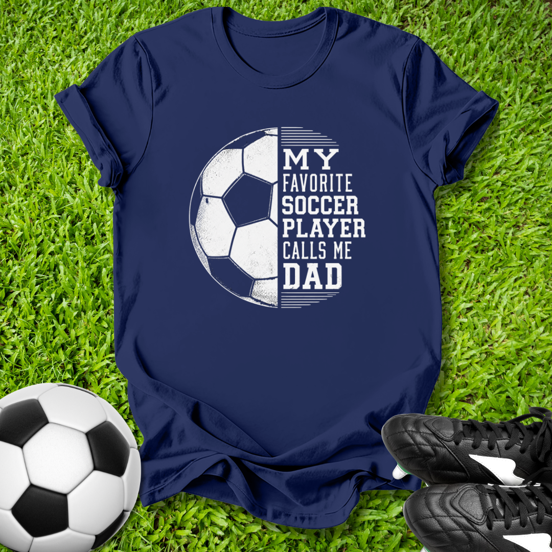 Navy blue t-shirt with soccer graphic and text on grass with soccer ball and shoes