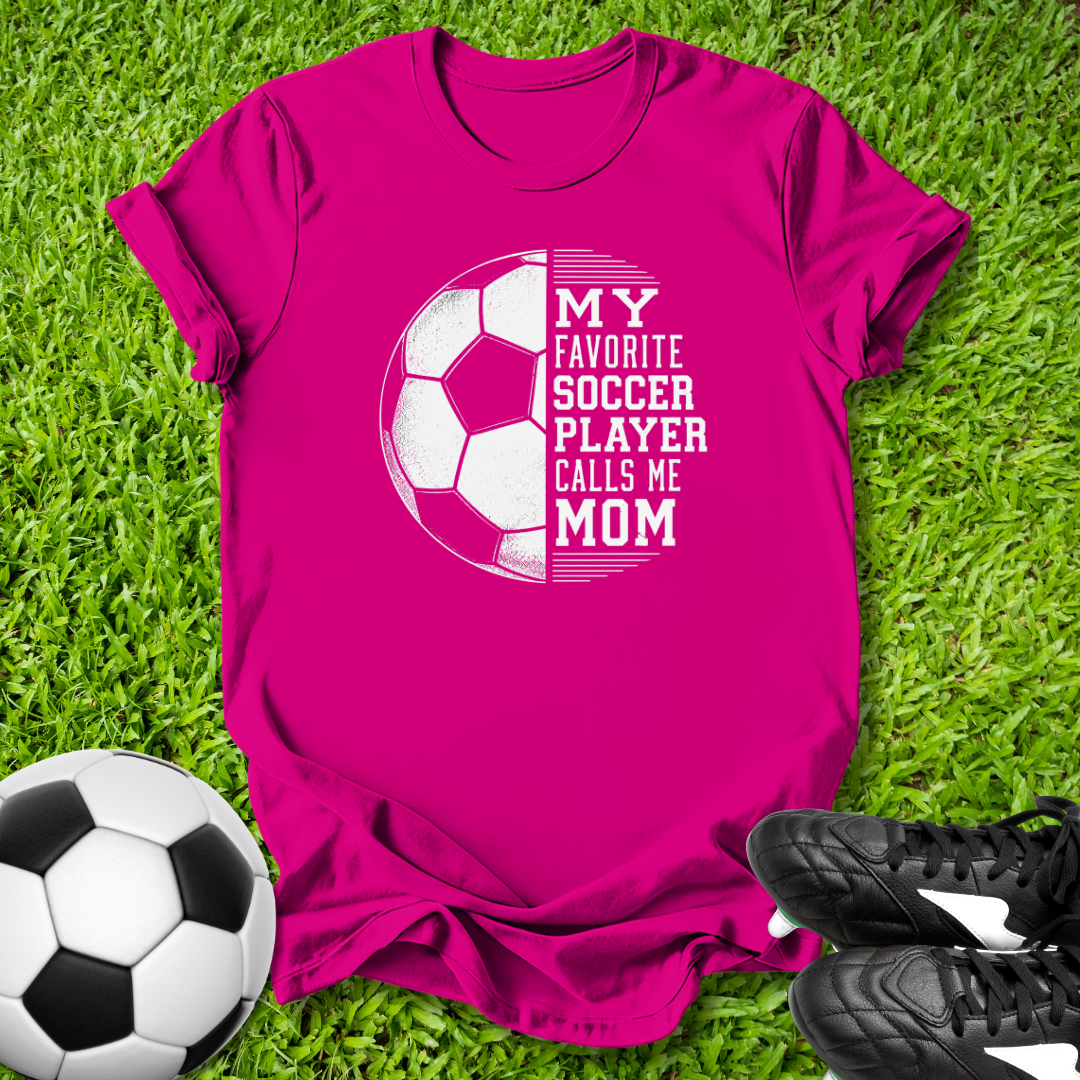 Pink t-shirt with soccer graphic and text on grass with soccer ball and shoes