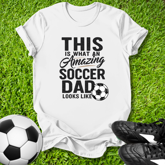 White Light blue t-shirt with 'This is what an amazing soccer dad looks like' text on grass with soccer ball and shoes.