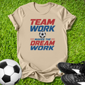 Beige t-shirt with 'Team Work Makes the Dream Work' text on grass with soccer ball and shoes.