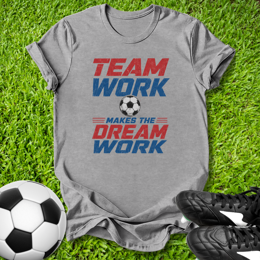 Gray t-shirt with 'Team Work Makes the Dream Work' text on grass with soccer ball and shoes.