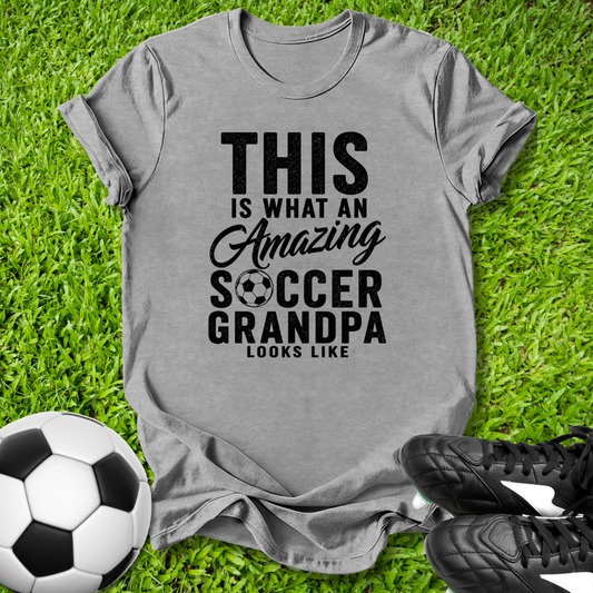 Gray t-shirt with 'Amazing Soccer Grandpa' text on grass with soccer ball and shoes.