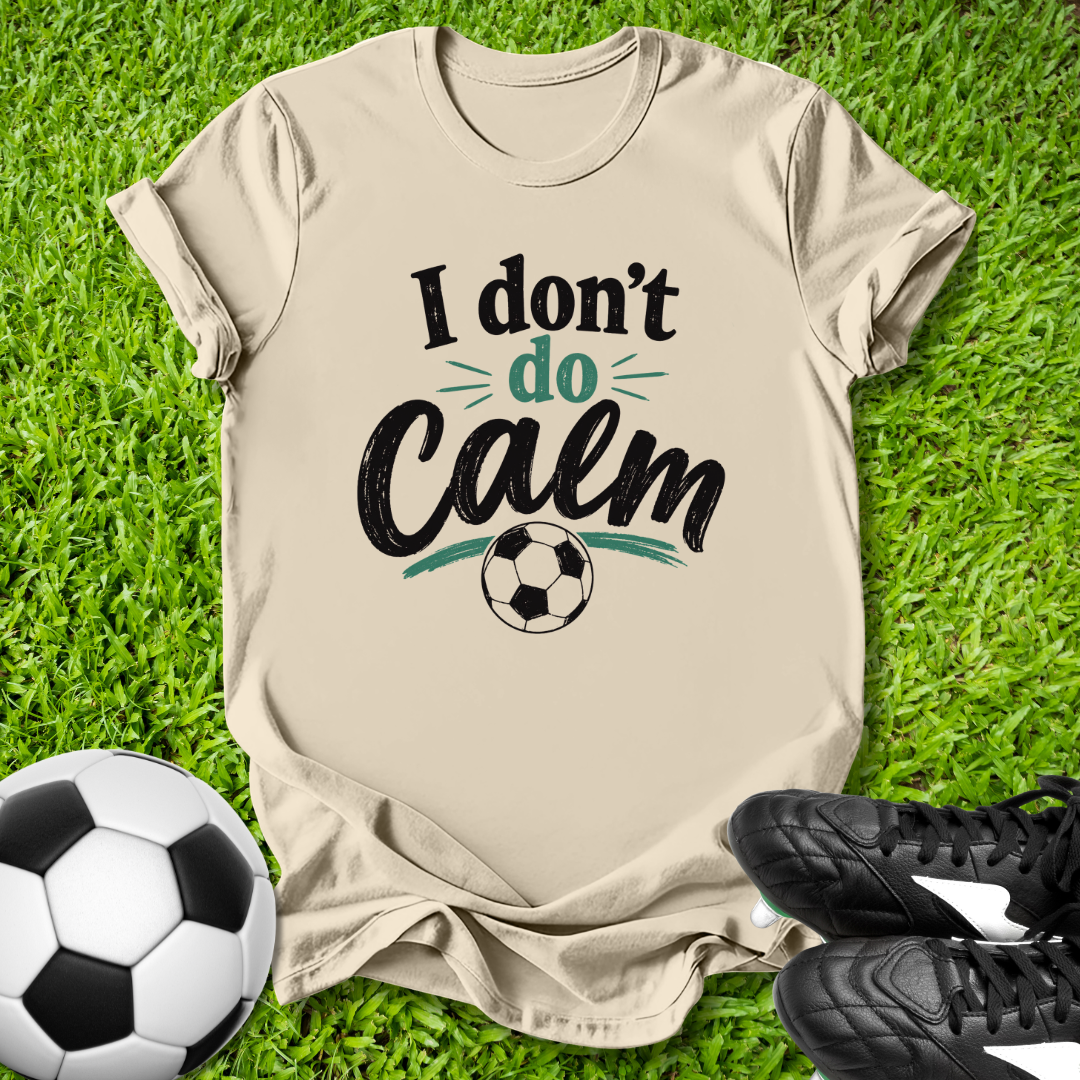Beige t-shirt with 'I don't do Calm' text and soccer ball on grass with soccer ball and shoes.