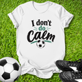 White t-shirt with 'I don't do Calm' text on grass with soccer ball and shoes