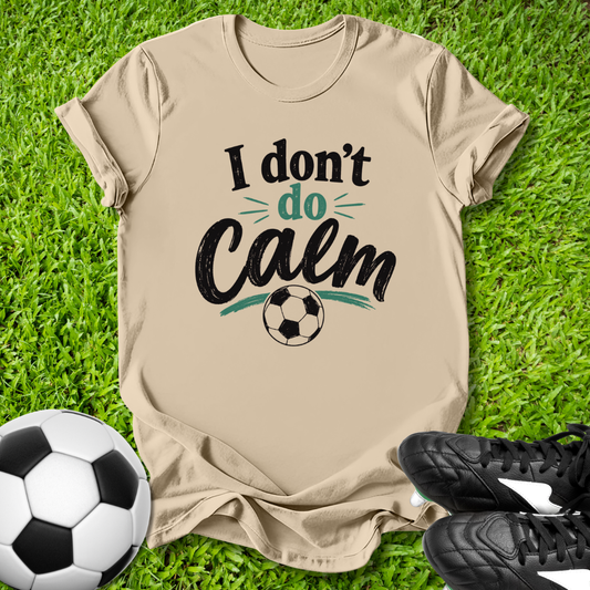 Beige t-shirt with 'I don't do Calm' text on grass with soccer ball and shoes