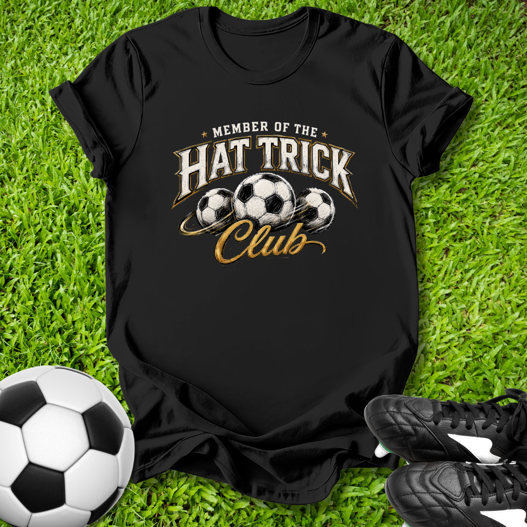 Black t-shirt with 'Member of the Hat Trick Club' design on grass with soccer ball and shoes.