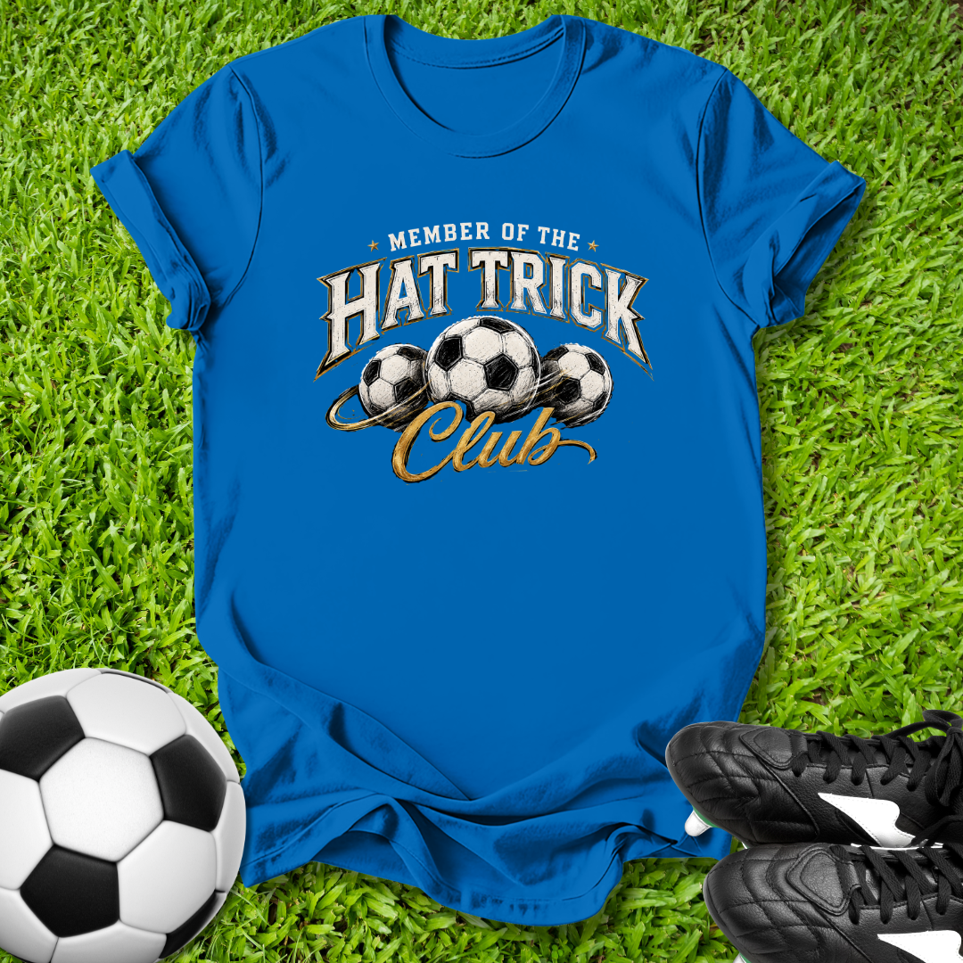 Blue t-shirt with 'Member of the Hat Trick Club' text and soccer balls on grass with a soccer ball and shoes.