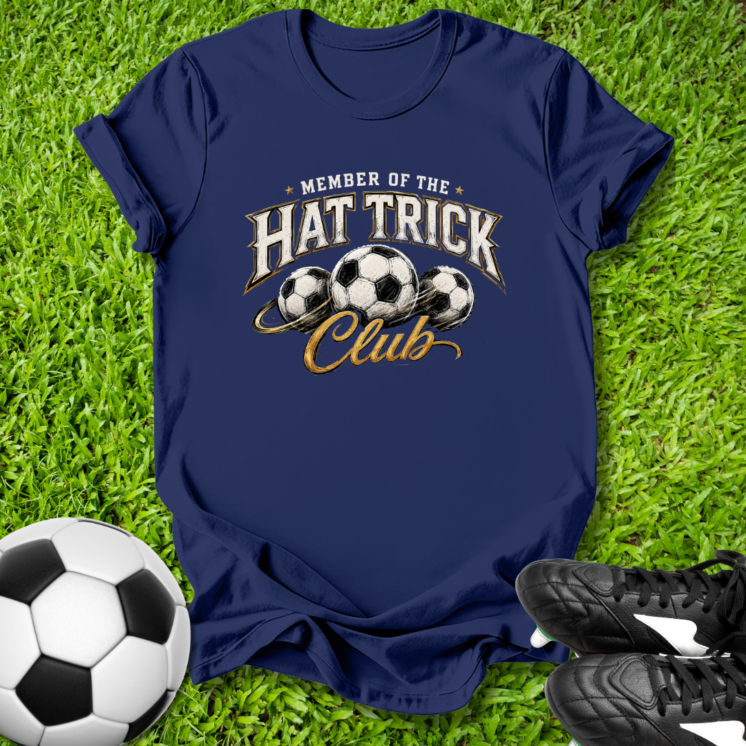 Navy blue t-shirt with 'Member of the Hat Trick Club' design on grass with soccer ball and shoes.
