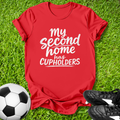 Red t-shirt with 'My second home has cupholders' text on grass with soccer ball and shoes.