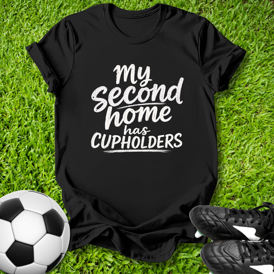 Black t-shirt with 'My second home has cupholders' text on grass with soccer ball and shoes.