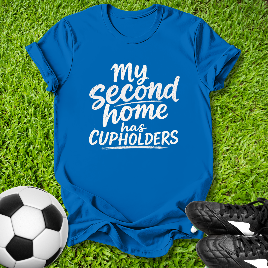 Blue t-shirt with 'My second home has cupholders' text on grass with soccer ball and shoes.