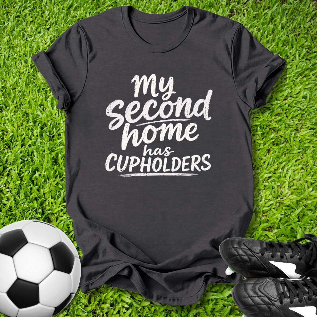 Black t-shirt with 'My second home has cupholders' text on grass with soccer ball and shoes.