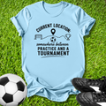 Light blue t-shirt with soccer-themed text on grass with soccer ball and shoes