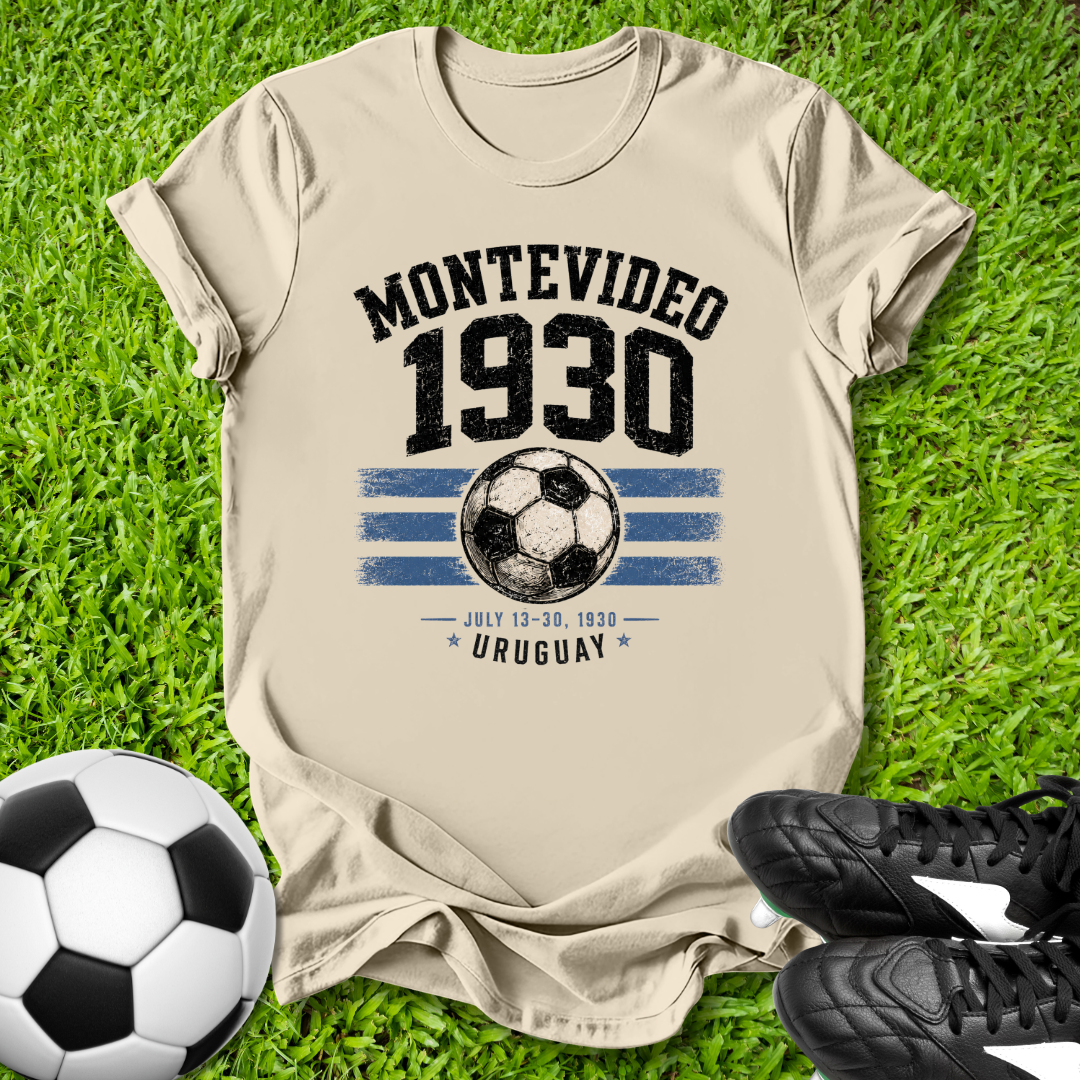Beige t-shirt with 'Montevideo 1930' design on grass with soccer ball and shoes.