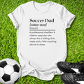 White t-shirt with 'Soccer Dad' definition on grass with soccer ball and shoes