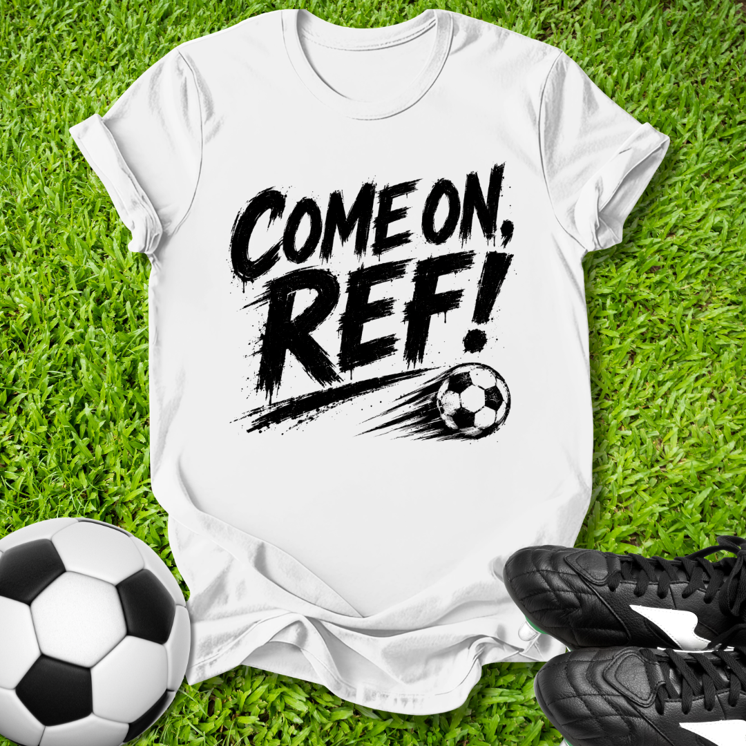 White t-shirt with 'COME ON, REF!' text on grass with soccer balls and shoes.