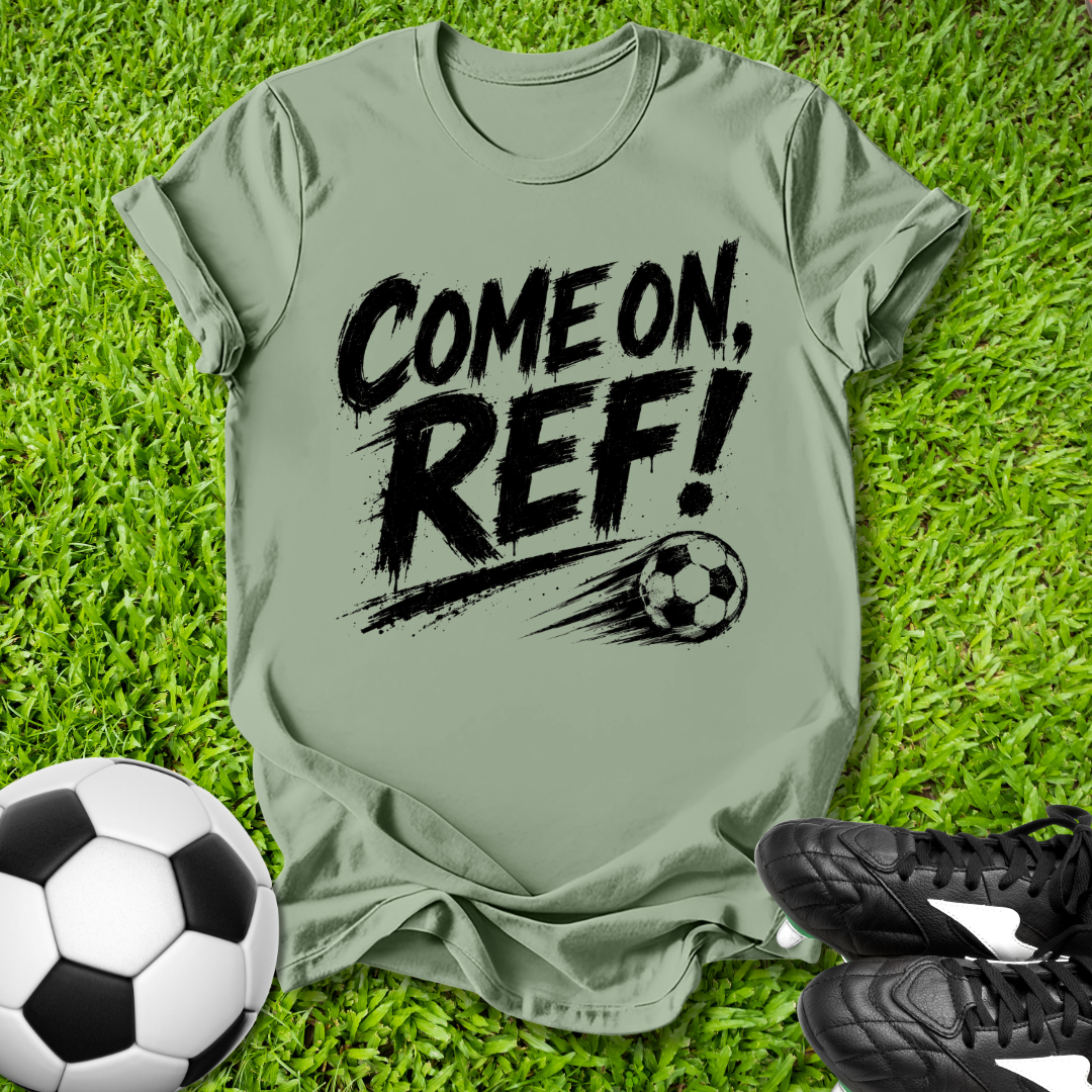 Green t-shirt with 'COME ON, REF!' text on grass with soccer ball and shoes.