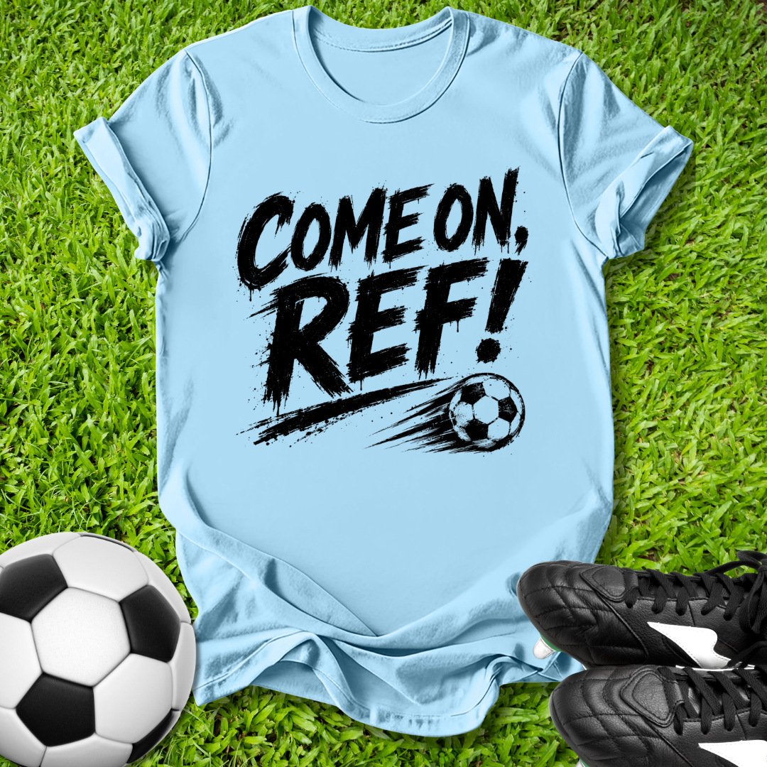 Light blue t-shirt with 'COME ON, REF!' text on grass with soccer ball and shoes.