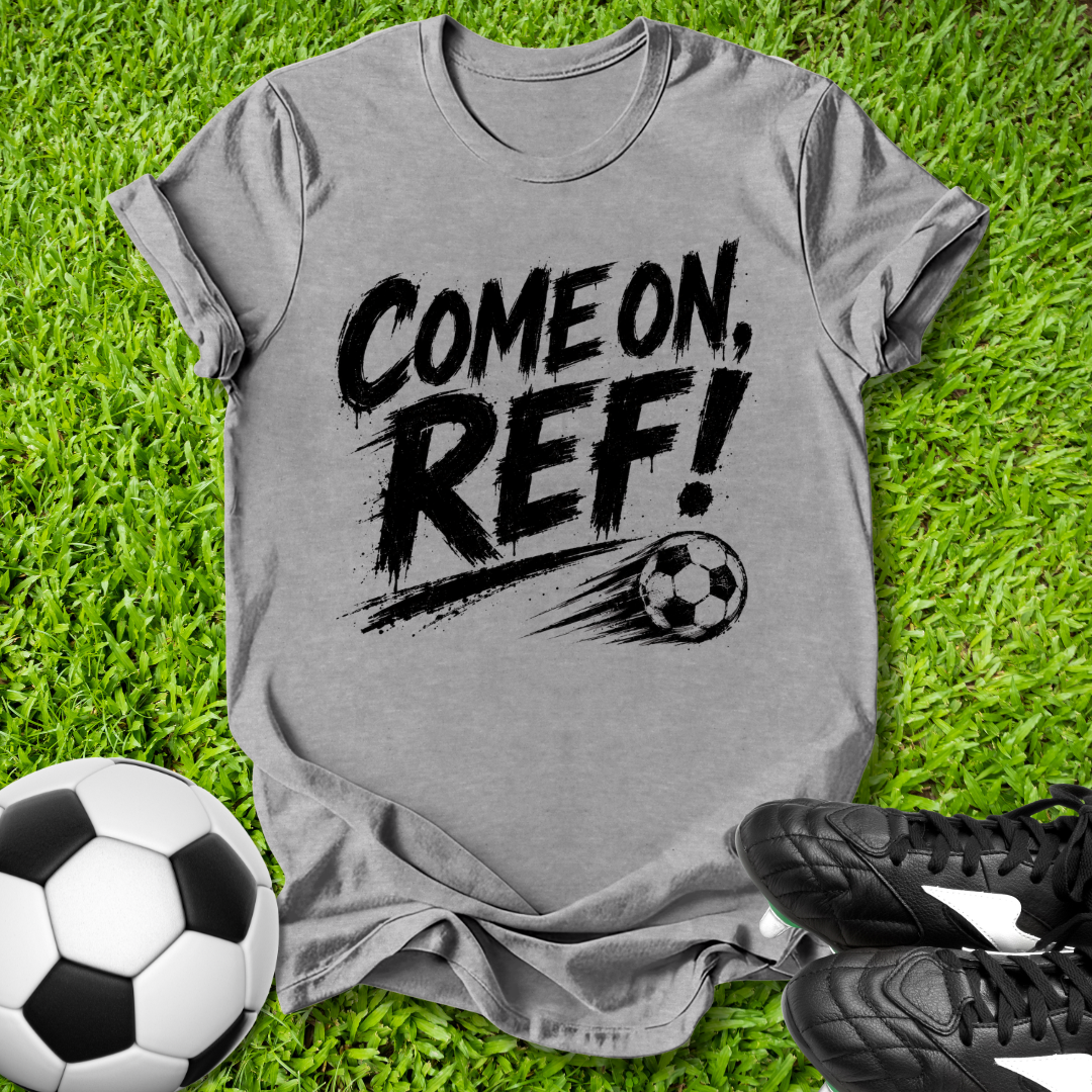 Gray t-shirt with 'COME ON, REF!' text on grass with soccer balls and shoes.