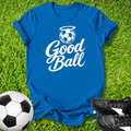 Blue t-shirt with 'Good Ball' design on grass with soccer ball and shoes