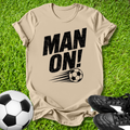 Beige t-shirt with 'MAN ON!' text and soccer ball graphic on grass with soccer ball and shoes.