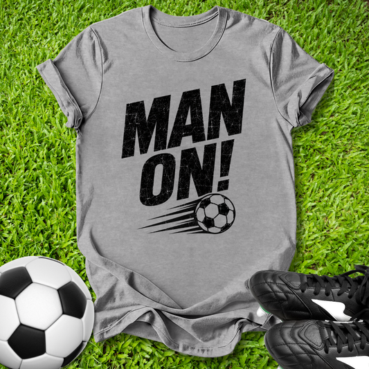 Gray t-shirt with 'MAN ON!' text and soccer ball graphic on grass with soccer ball and shoes.