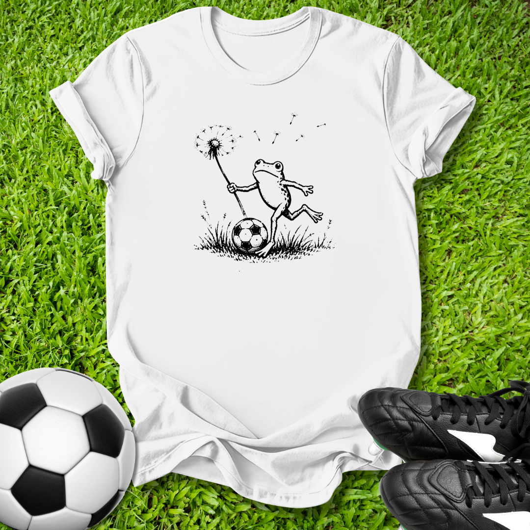 White t-shirt with a frog graphic on grass with soccer ball and shoes