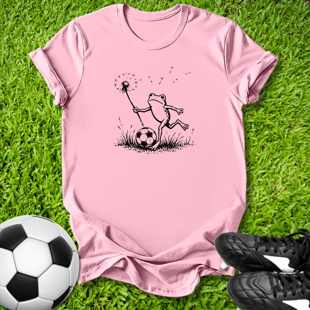 Pink t-shirt with a frog graphic on grass with soccer ball and shoes