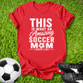 Red t-shirt with 'Amazing Soccer Mom' text on grass with soccer ball and shoes